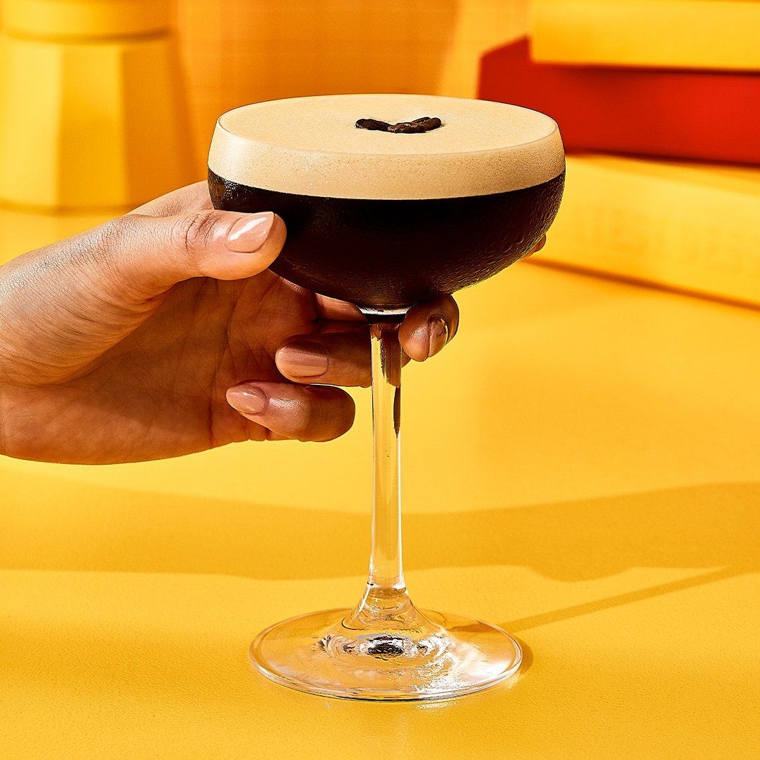 Hand holding espresso martini against a yellow background