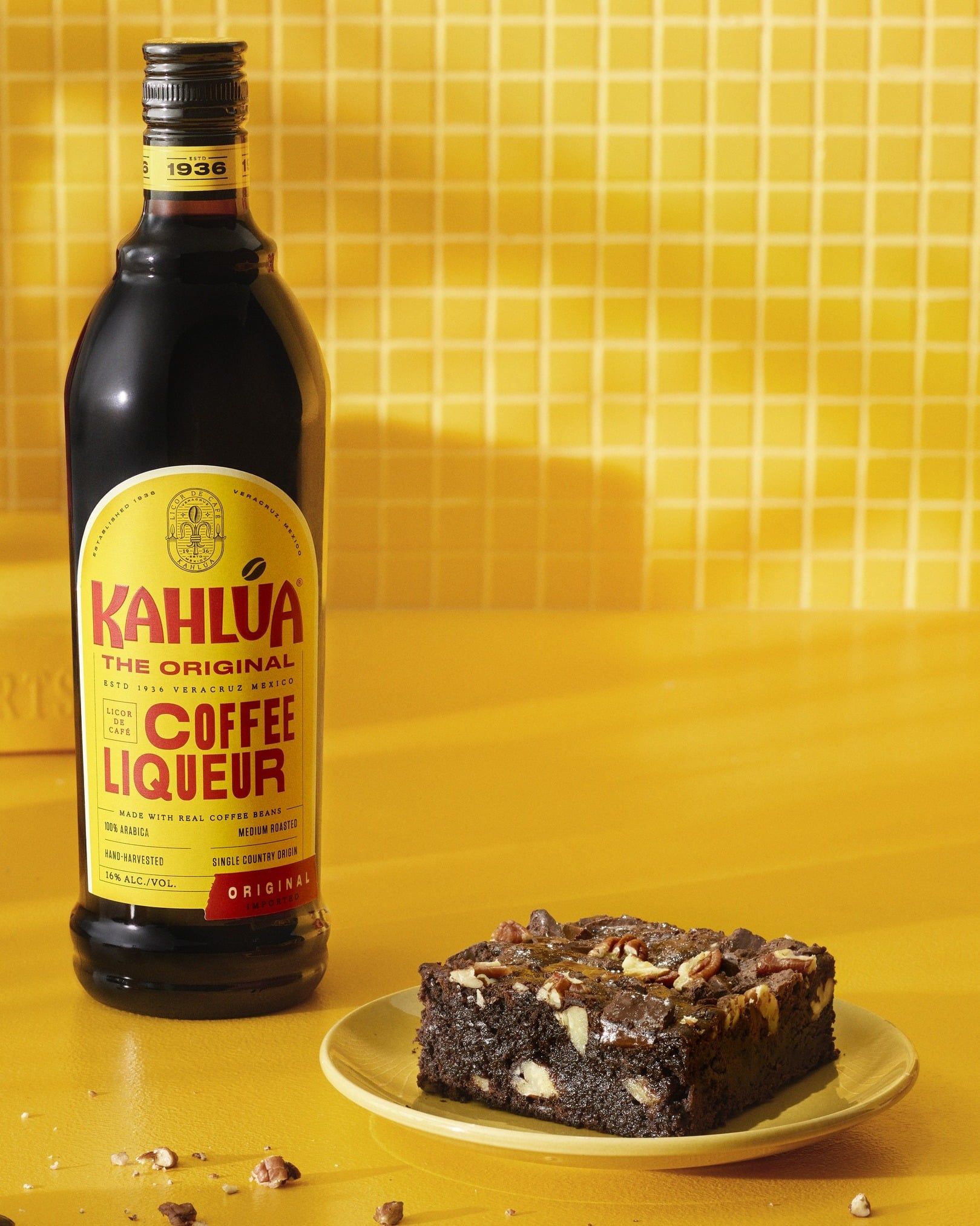 A bottle of Kahlua and a cake on a place in a yellow kitchen