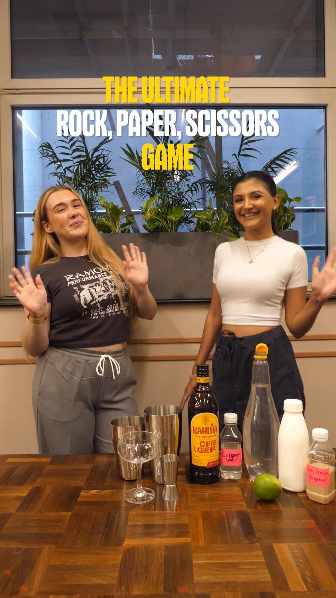 Two girls playing a game of rock, paper, scissors with cocktail ingredients on the table