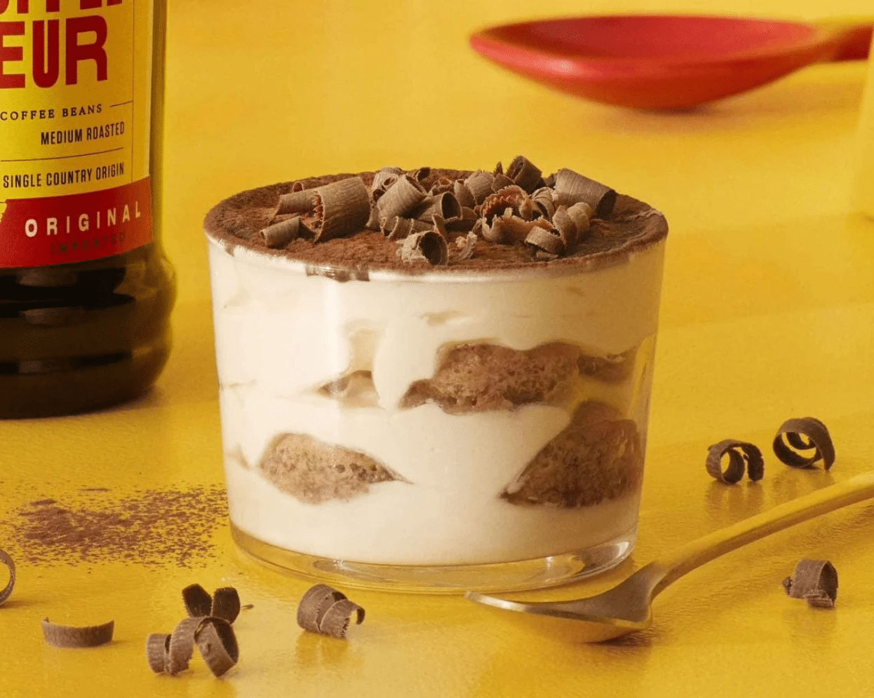 One tiramisu desert garnished with chocolate in front of a yellow background